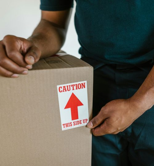 A person handling a moving box with a 'caution this side up' label indoors.